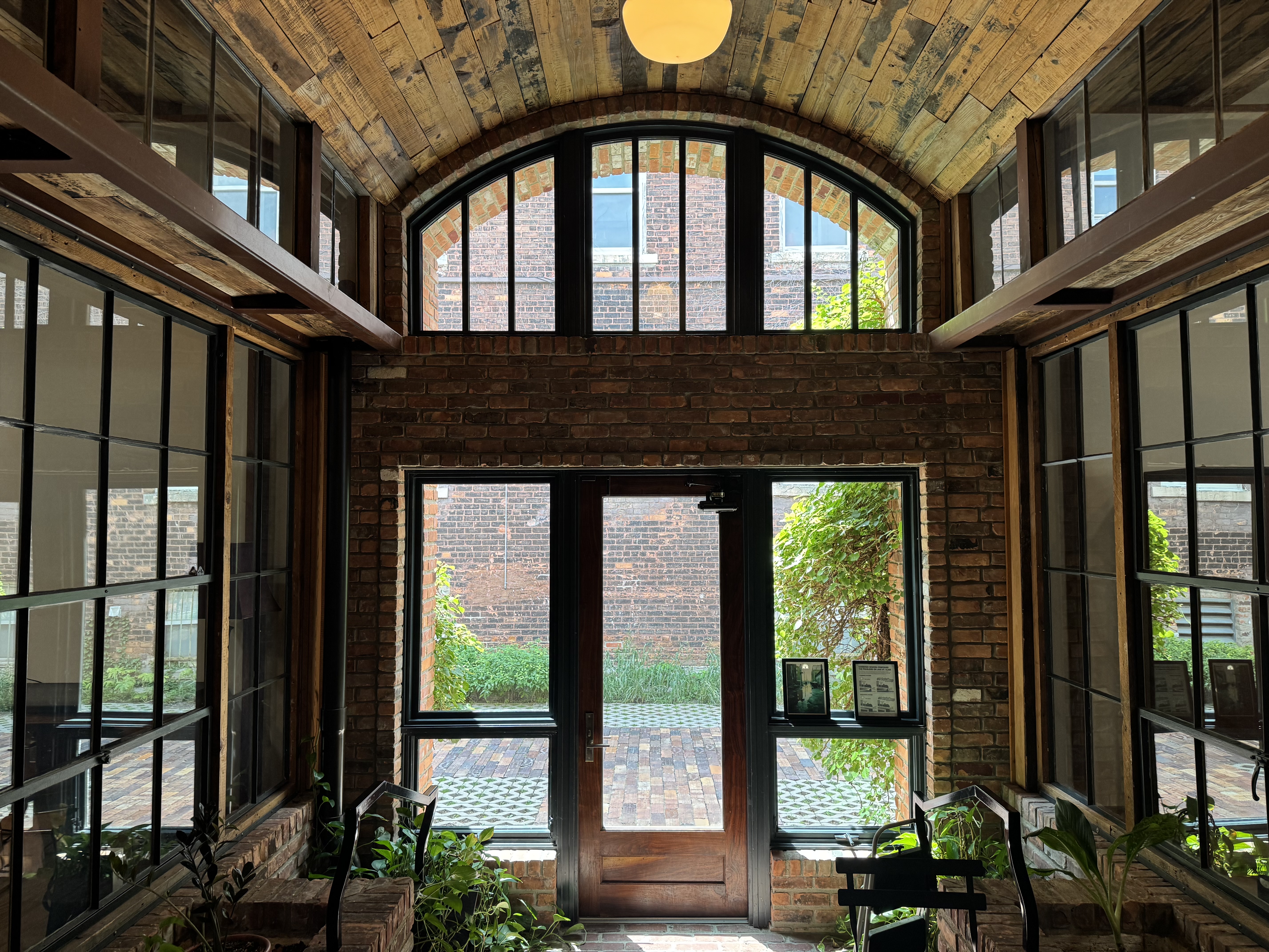 A glass-enclosed room is shown filled with plants and a bistro seating set.